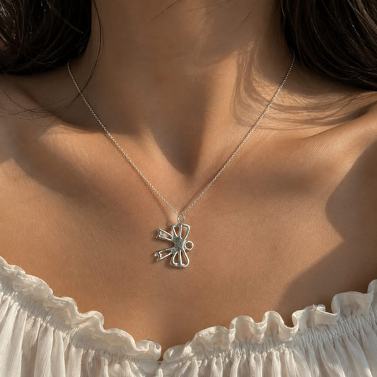 925 Sterling Silver Ribbon Bow Charm Pendant Resting on a Neutral Ceramic Dish