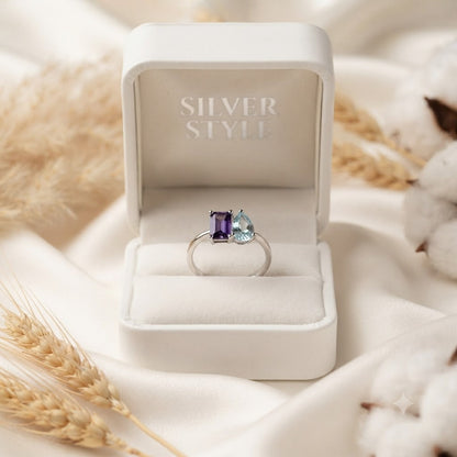 Twin Amethyst and Blue Topaz Ring crafted in 925 Sterling Silver featuring an emerald cut Amethyst and heart cut Blue Topaz gemstone.