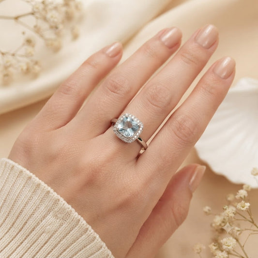 Halo Blue Topaz Ring crafted in 925 Sterling Silver with a cushion cut sky blue gemstone surrounded by a sparkling halo in a four-prong setting.
