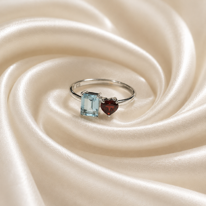 Twin Blue Topaz and Garnet Ring crafted in 925 Sterling Silver featuring an emerald cut Blue Topaz and heart cut Garnet gemstone.