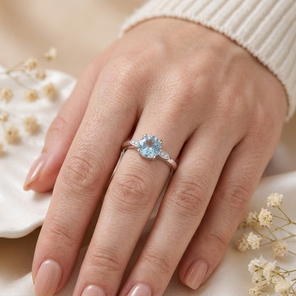 Solitaire Blue Topaz Ring crafted in 925 Sterling Silver with a round cut sky blue gemstone and four-prong setting with accent stones on the shoulders.