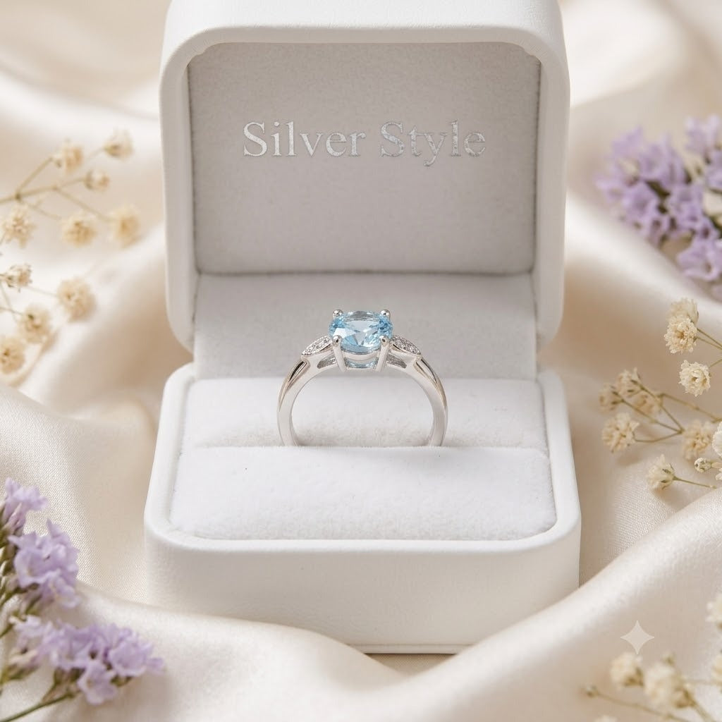 Solitaire Blue Topaz Ring crafted in 925 Sterling Silver with a round cut sky blue gemstone and four-prong setting with accent stones on the shoulders.