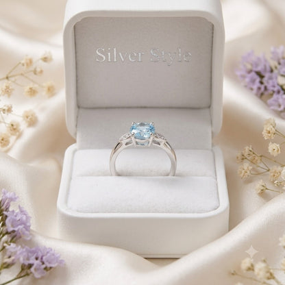 Solitaire Blue Topaz Ring crafted in 925 Sterling Silver with a round cut sky blue gemstone and four-prong setting with accent stones on the shoulders.