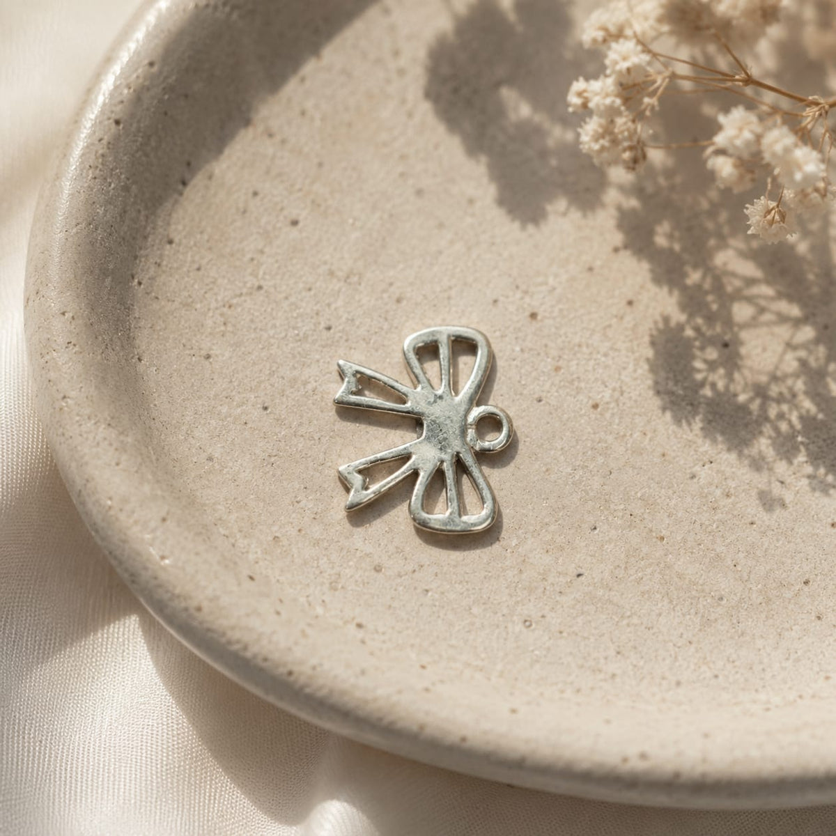 925 Sterling Silver Ribbon Bow Charm Pendant Resting on a Neutral Ceramic Dish