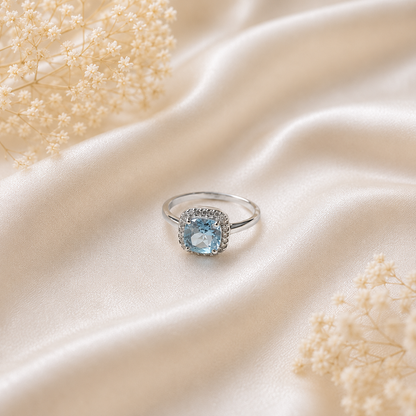 Halo Blue Topaz Ring crafted in 925 Sterling Silver with a cushion cut sky blue gemstone surrounded by a sparkling halo in a four-prong setting.